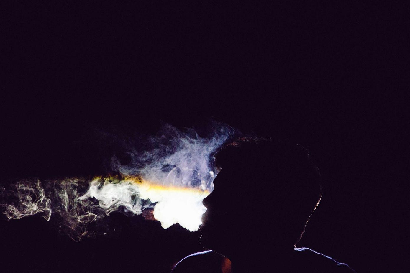 Silhouette of a person exhaling a cloud of glowing smoke.