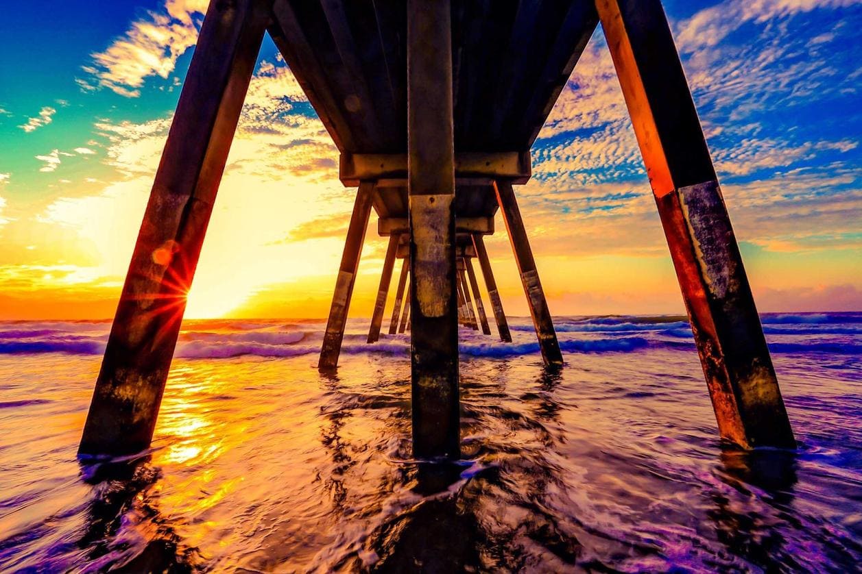 Golden sunrise seen from under a pier over ocean waves.